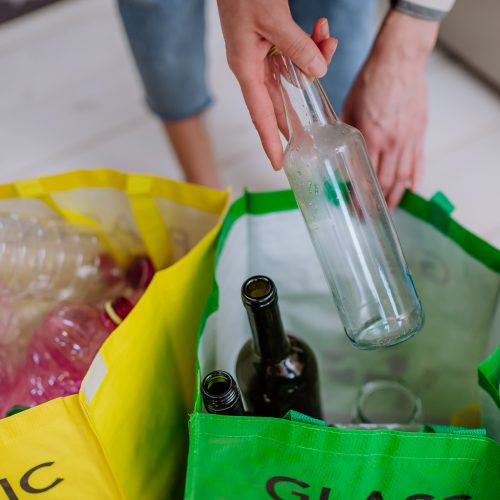 Midsection of a woman throwing empty glass bottle in recycling bin in kitchen.