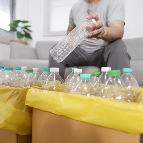 Home recycle eco green zero concept Man throwing empty plastic bottle in recycling bin with yellow garbage bags at home.